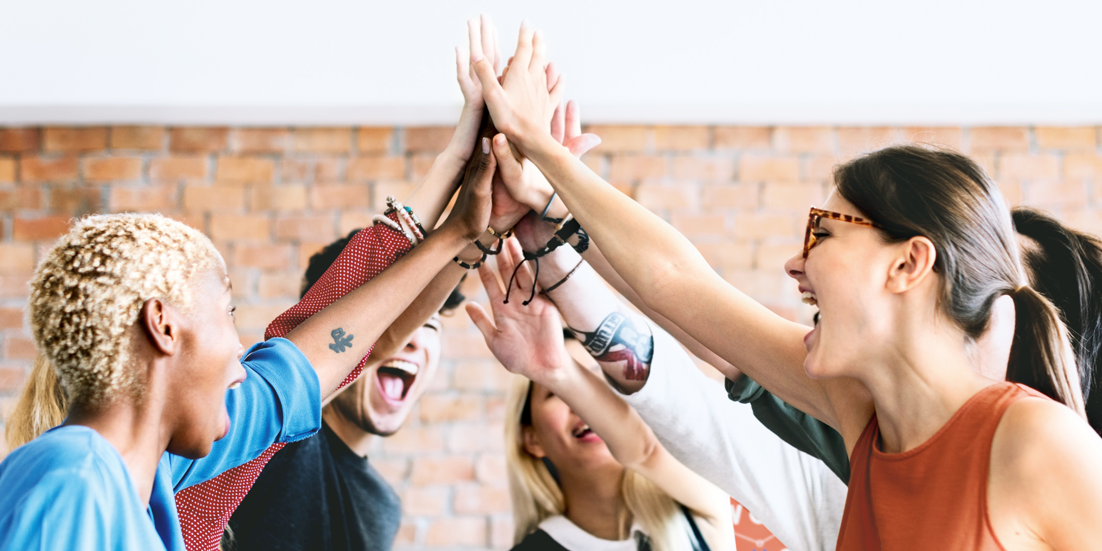 Mehrere Menschen stehen im Kreis, sie lachen und geben sich ein gemeinsames High Five.